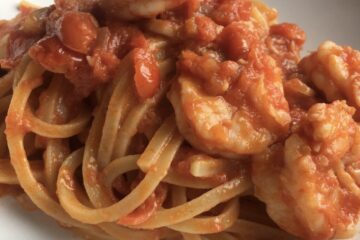 shrimp pasta in red sauce piled high on top of triangular spaghetti noodles in a white pasta bowl