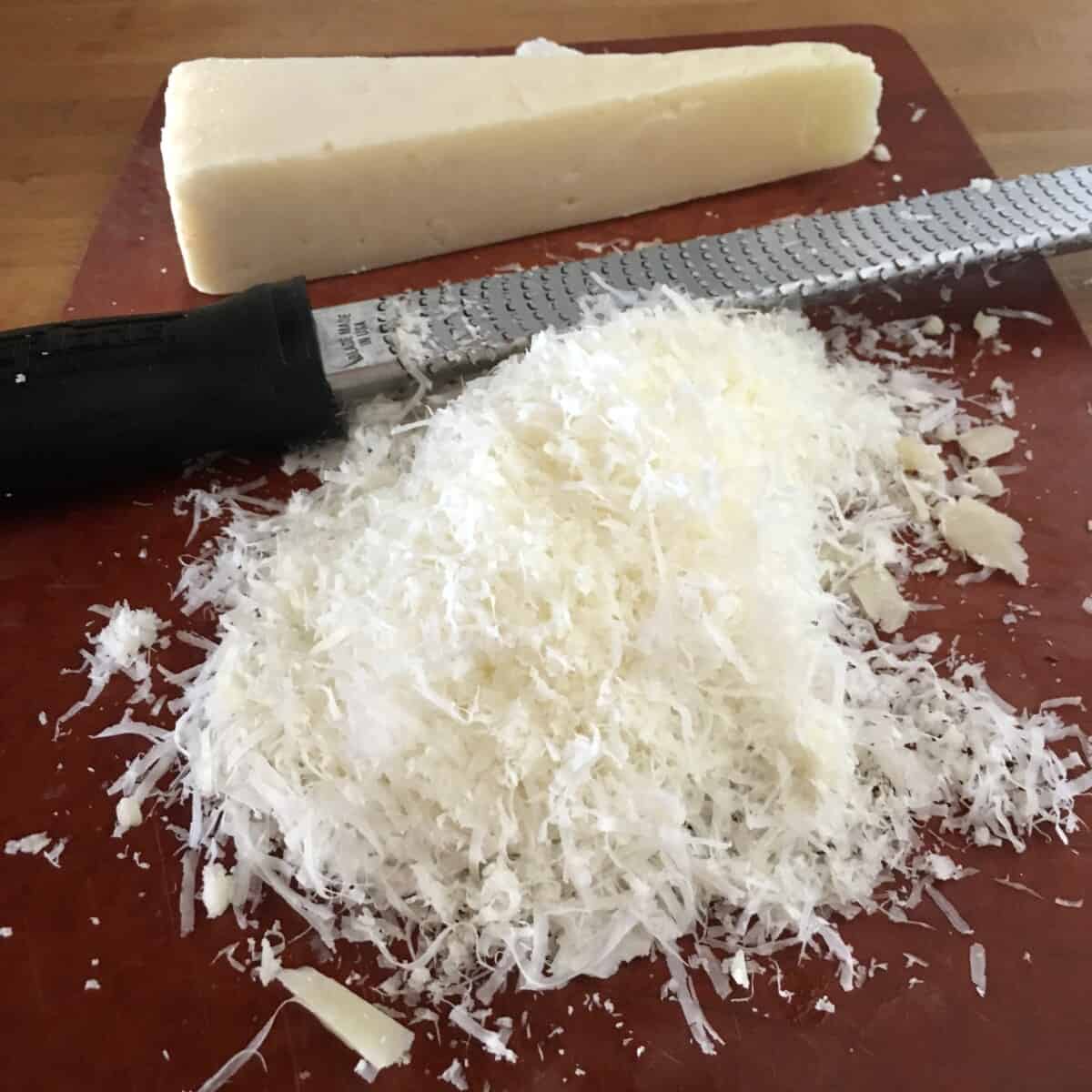 a pile of snow white grated pecorino cheese next to a microplane and cheese wedge