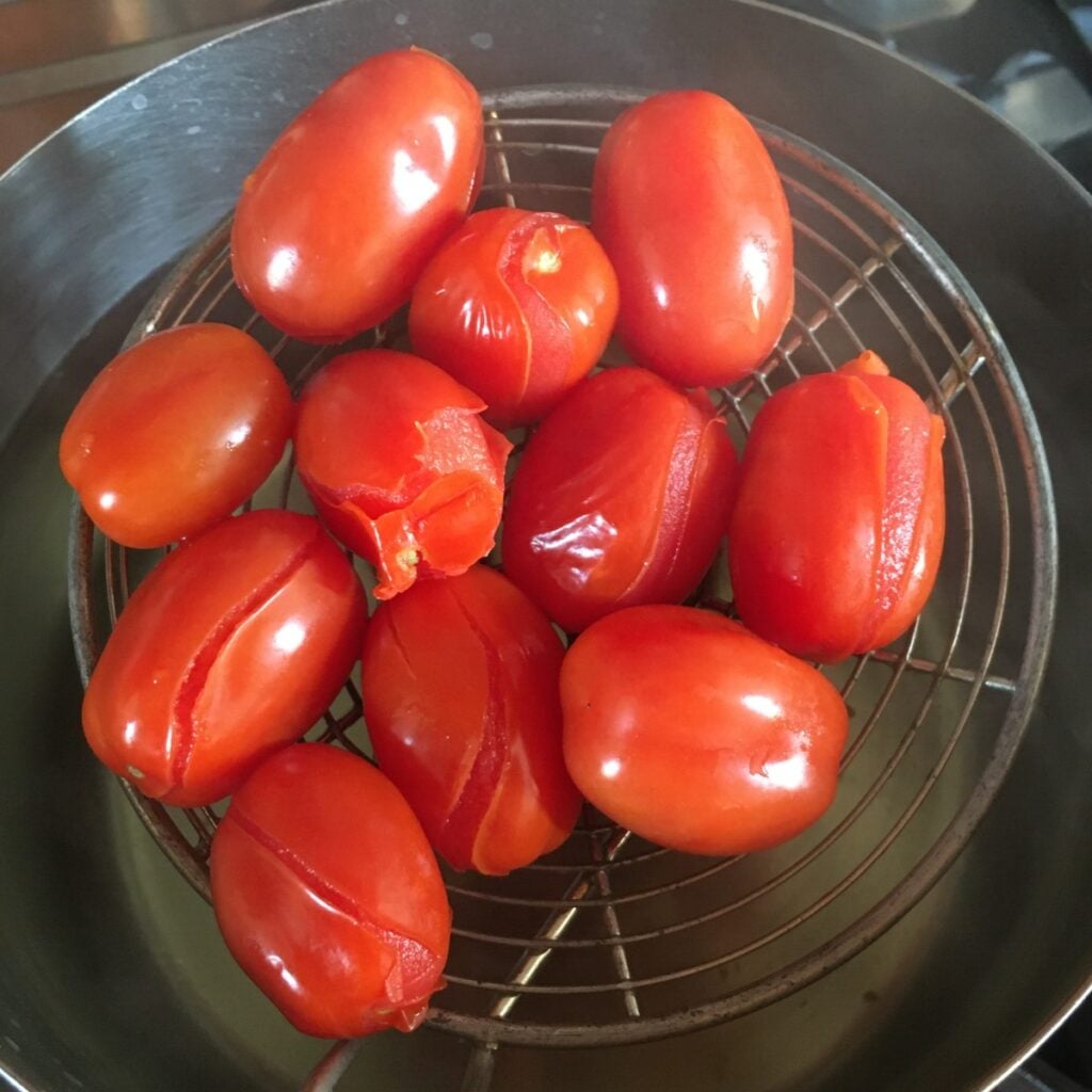 blanched grape tomatoes in a spider strainer with skins starting to peel off