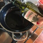 my hand pouring a bottle of olive oil into the skillet
