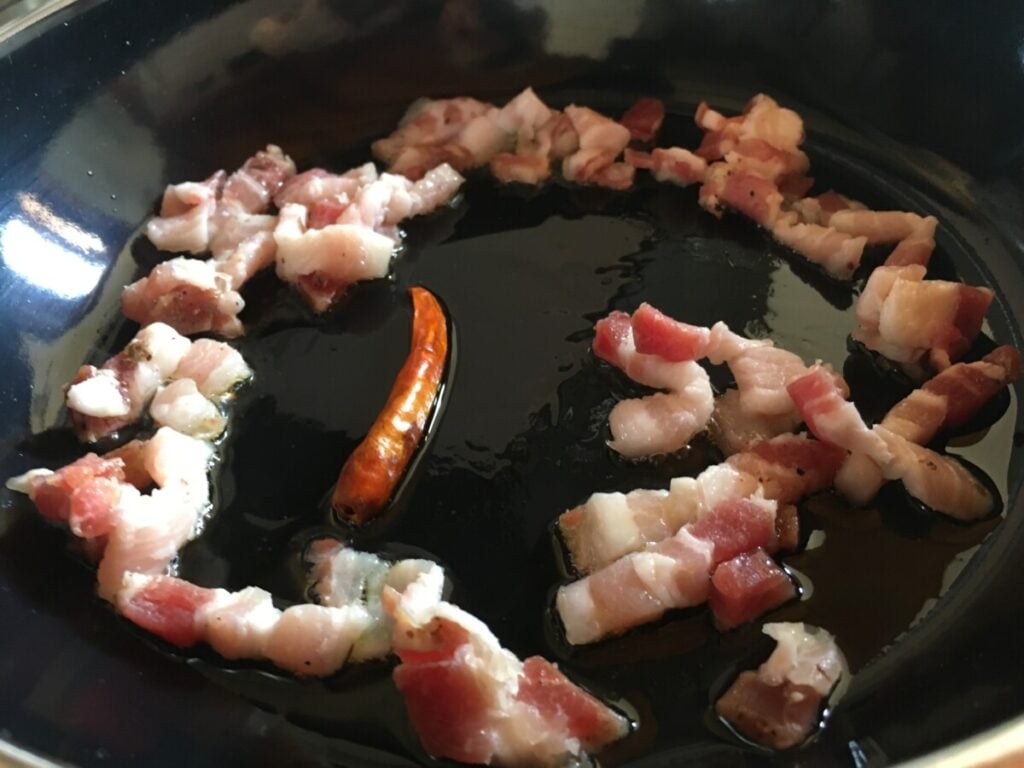 Pancetta cooking in skillet with chili pepper and olive oil
