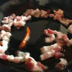 pancetta pieces cooking in the skillet with the chili pepper and olive oil