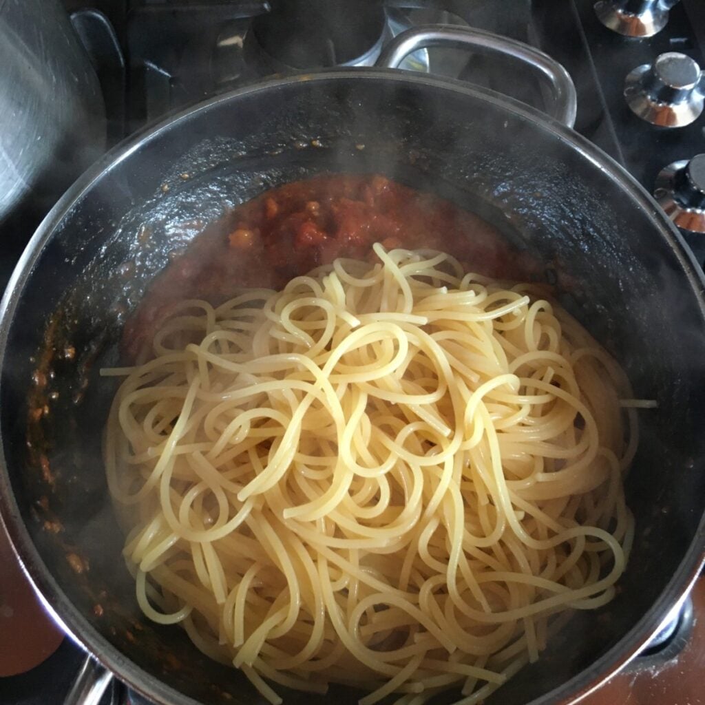 Adding strained pasta to amatriciana sauce