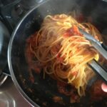 using tongs to coat the pasta noodles with sauce