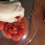 my hand squeezing the grape tomatoes between my fingers to crush them