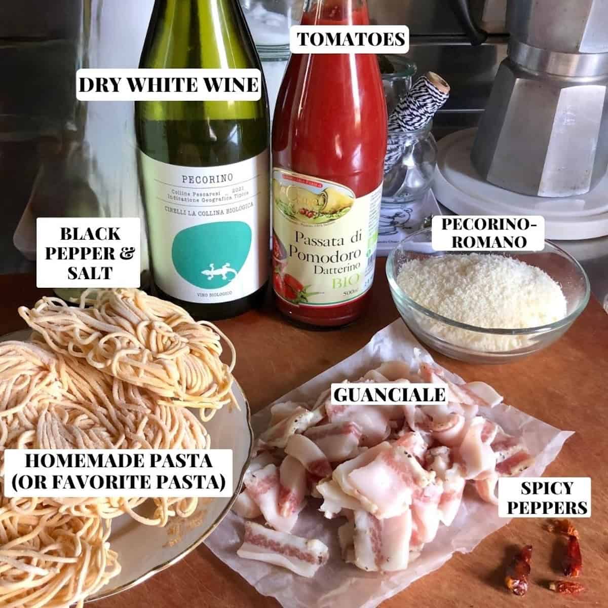 Traditional amatriciana ingredients on cutting board including guanciale, pecorino romano, tomatoes, dried spicy peppers, white wine, and pasta for authentic amatriciana sauce recipe.
