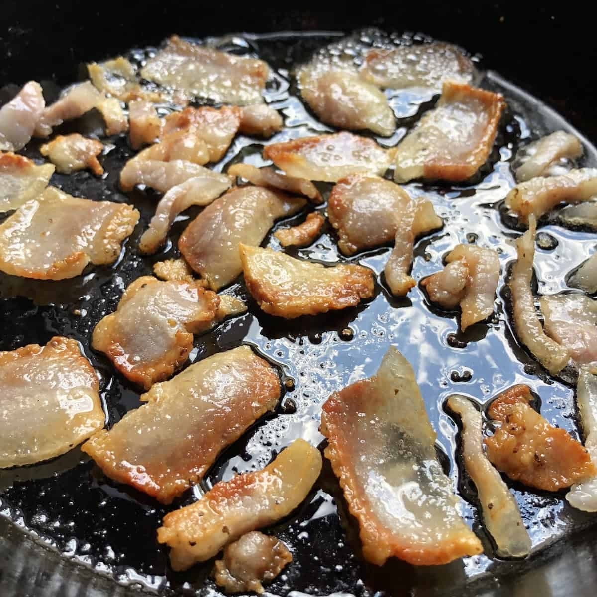 Shiny, glistening fatty golden brown crispy guanciale cooking in cast iron skillet rendering fat, showing how to cook guanciale for amatriciana or gricia pasta recipe.
