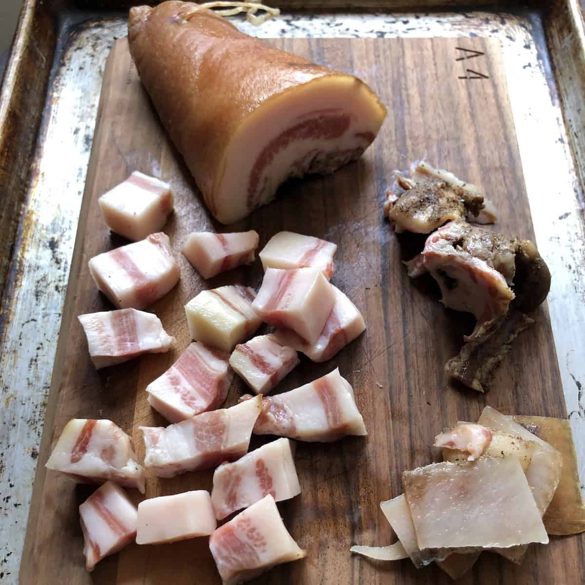Whole rolled guanciale slab with cubed chopped pieces on cutting board showing how to trim the skin and the seasonings off of the guanciale before cutting this Italian cured pork jowl for amatriciana, carbonara, or gricia pasta.

