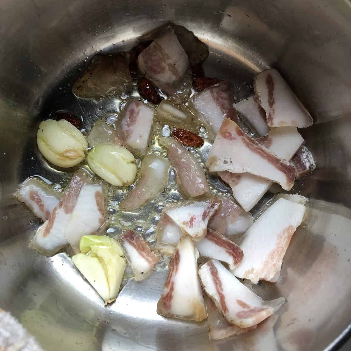 Guanciale rendering with garlic cloves and dried red peppers in pot, non-traditional amatriciana sauce recipe variation for customized pasta amatriciana.
