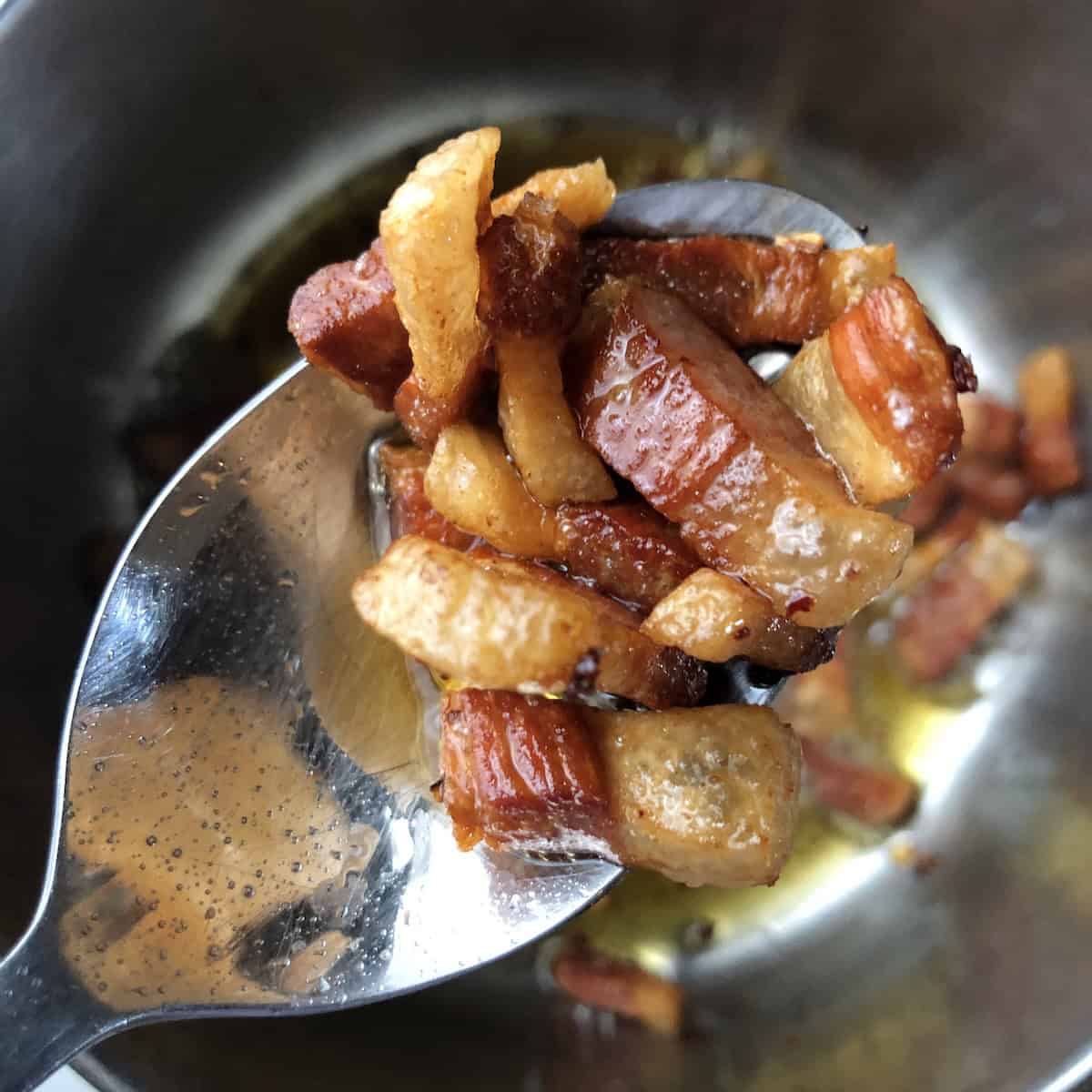 Spoonful of perfectly cooked tender guanciale, ideal texture for amatriciana, carbonara, or gricia pasta recipes.
