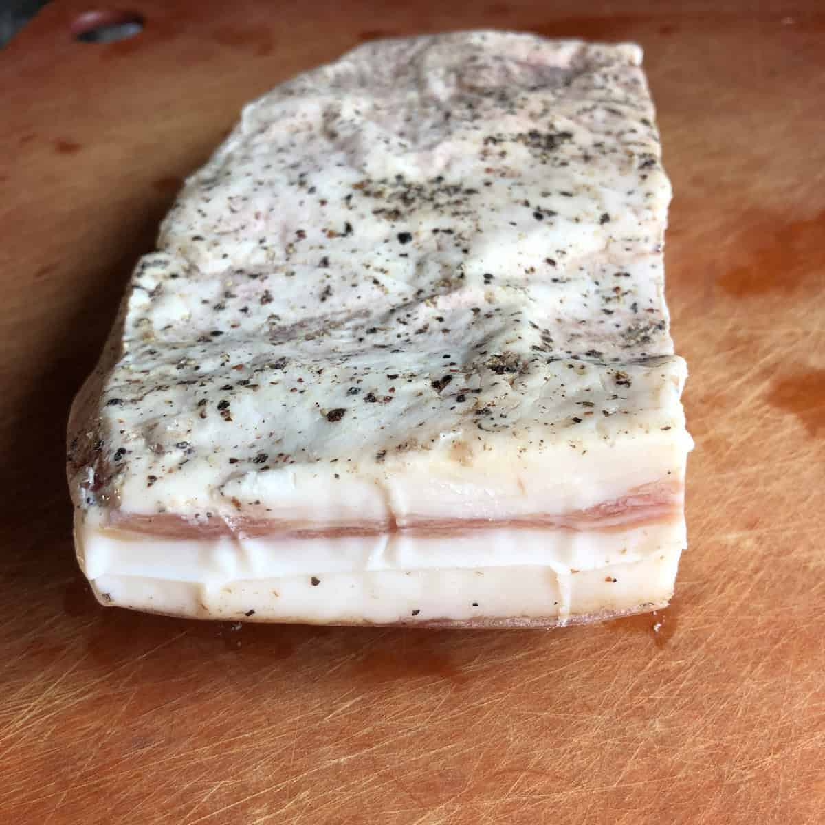 Seasoned guanciale slab showing cured meat and fat side, authentic Italian pork jowl for carbonara sauce, gricia pasta sauce, and amatriciana pasta recipes.

