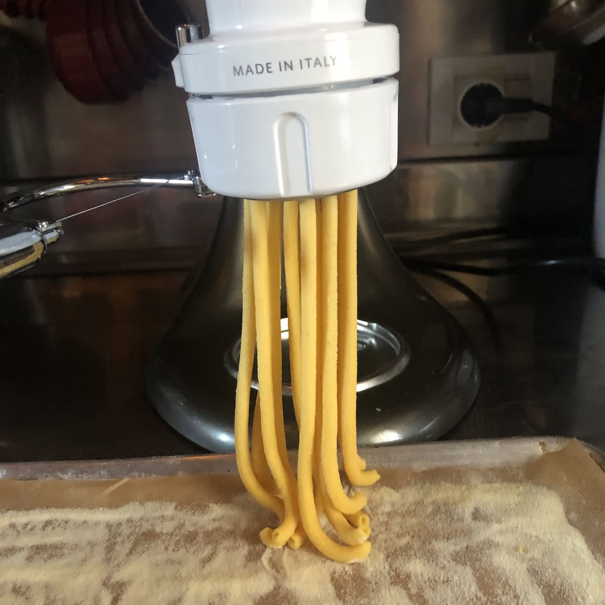 Homemade bucatini pasta extruding from KitchenAid pasta attachment showing hollow hole, how to make bucatini for amatriciana or carbonara.
