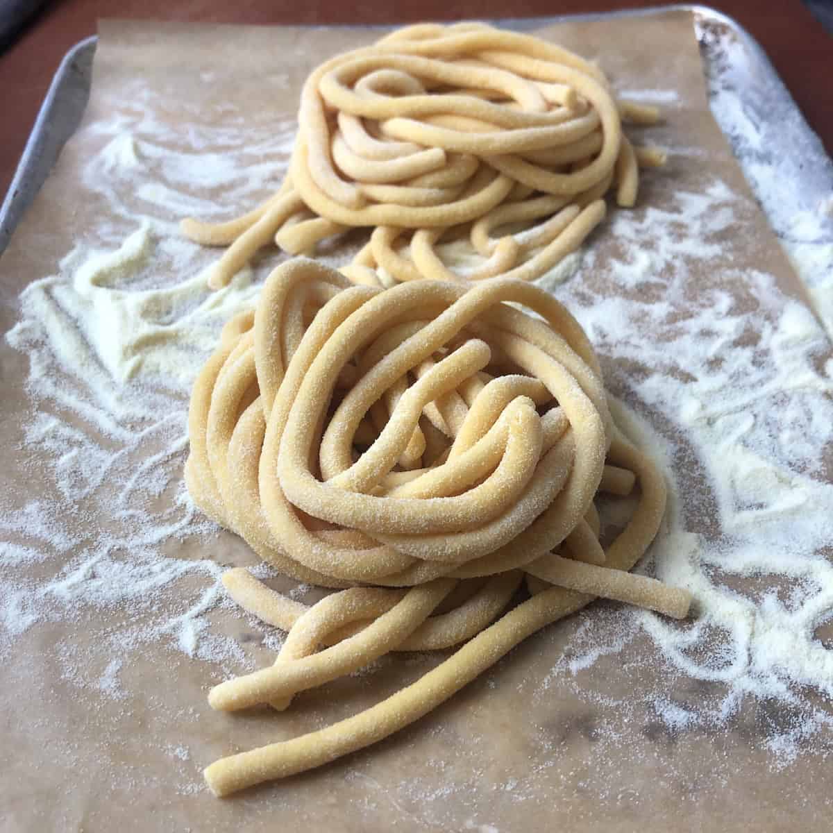 Homemade bucatini pasta nests on parchment lined sheet tray dusted with semolina rimacinata, fresh pasta for bucatini all'amatriciana recipe.
