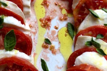 two lines of alternating tomato and mozzarella slices drizzled with bright green olive oil, sea salt and sprinkled with baby leaves of basi.