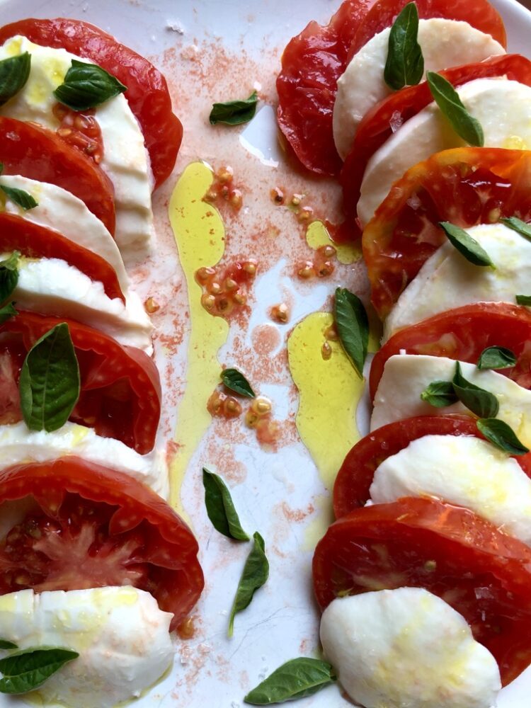 two lines of alternating tomato and mozzarella slices drizzled with bright green olive oil, sea salt and sprinkled with baby leaves of basi.