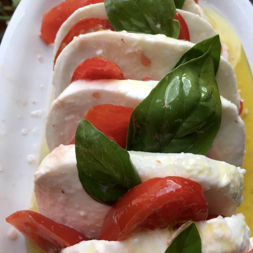 beautiful caprese salad with leaves of basil and grape tomatoes tucked in between each slice of thick milky mozzarella
