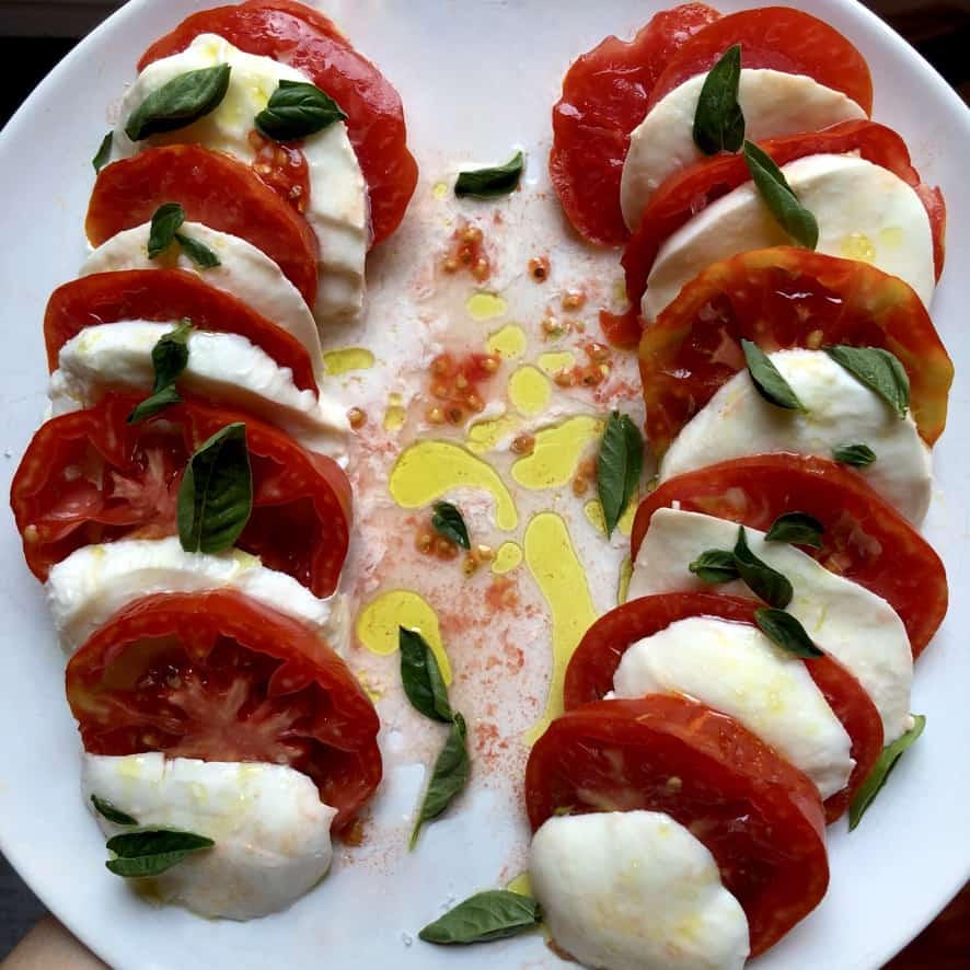 beautiful caprese salad for two on a white platter with the reddest tomatoes and the brightest green extra virgin olive oil