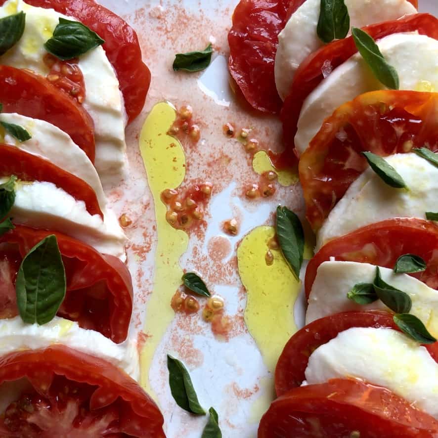 beautiful caprese salad for two on a white platter with the reddest tomatoes and the brightest green extra virgin olive oil