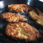 perfectly fried panko-crusted golden brown chicken breast still cooking in a cast iron skillet