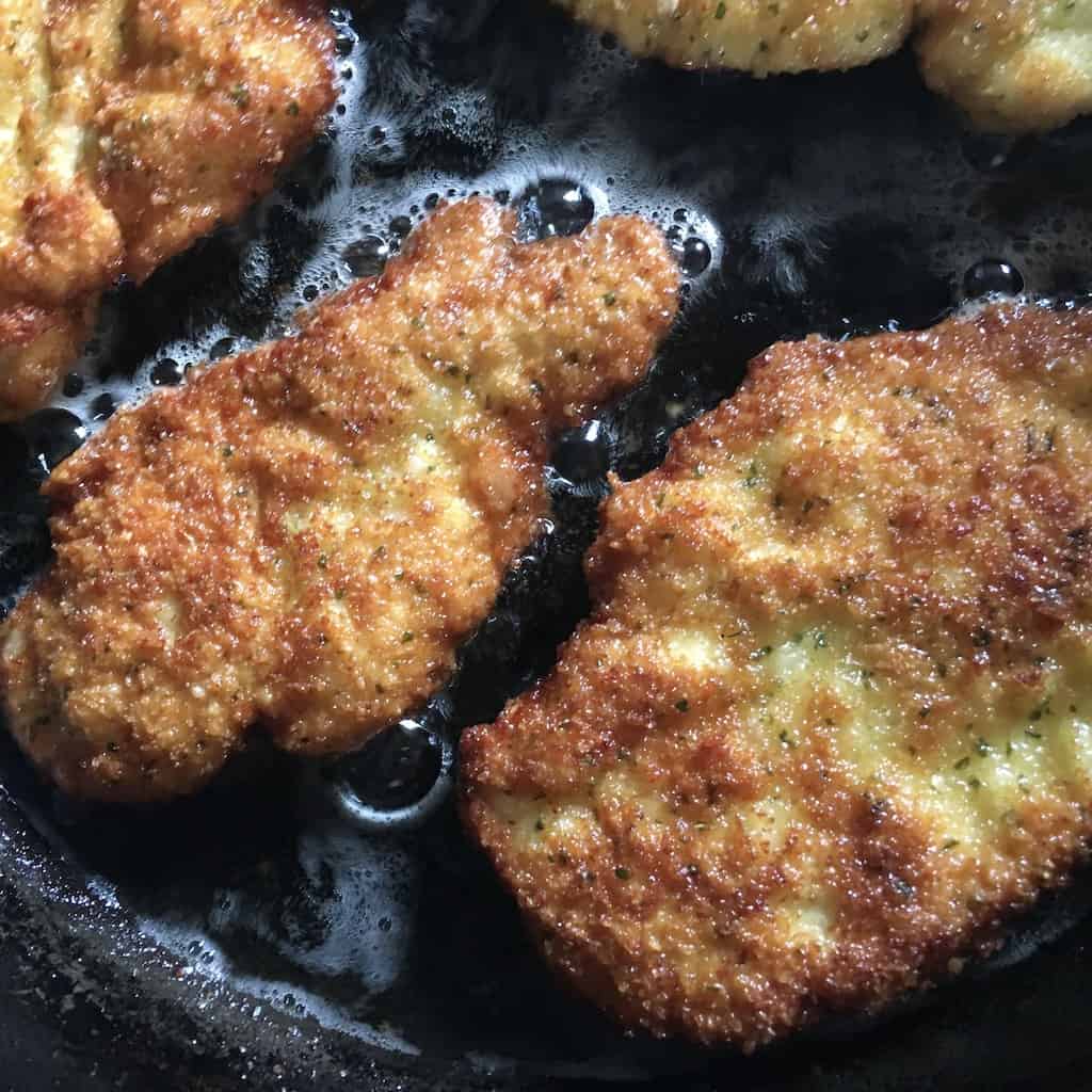 perfectly fried panko-crusted golden brown chicken breast still cooking in a cast iron skillet