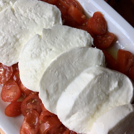 thick milky luscious slices of mozzarella lying on top of a bed of datterino grape tomatoes on a white platter