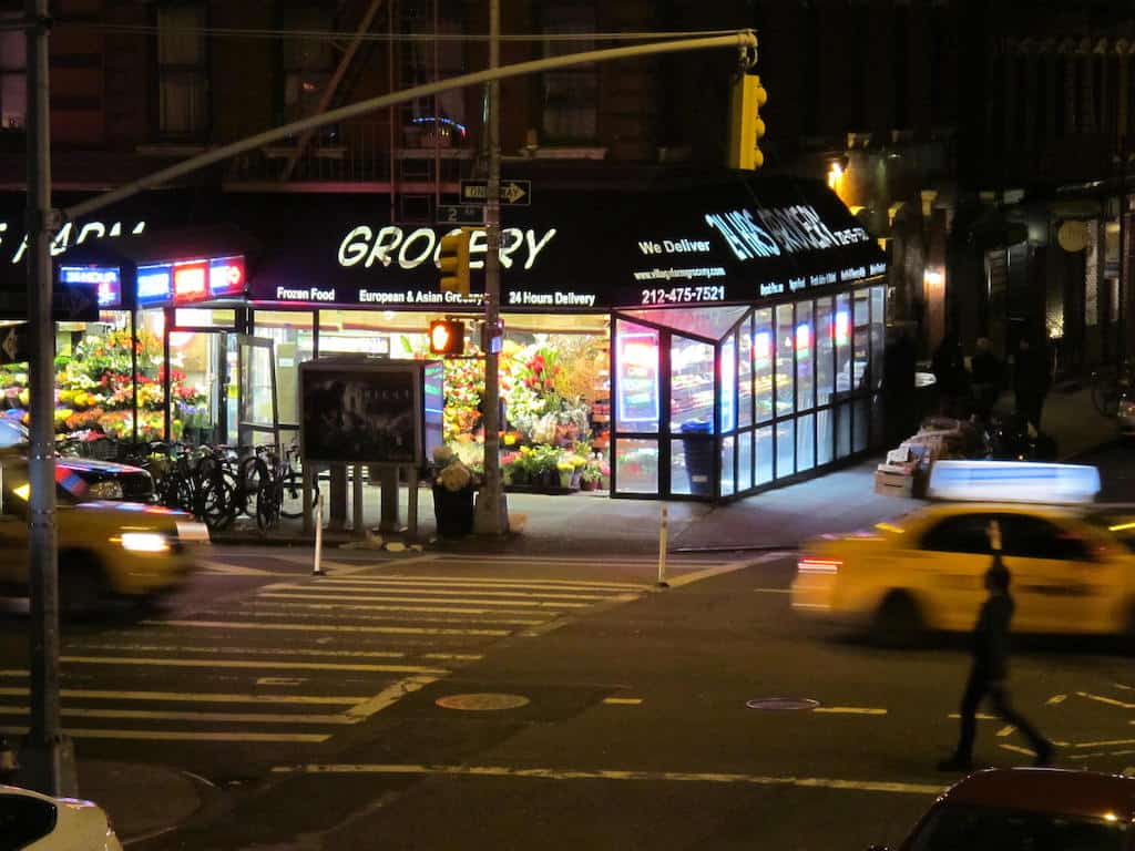 photo view taken from my balcony at night on a busy intersection with my corner deli and grocer in the background with neon lights and taxis driving by