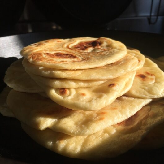 a stack of naan bread inside a cast iron skillet with the sun drenching the bread