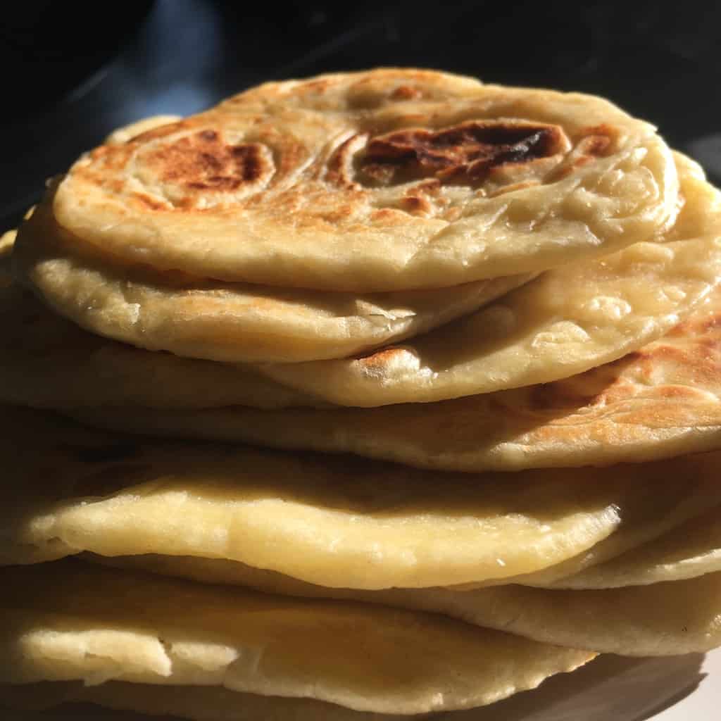 stack of beautiful fluffy naan bread with the sun beating down on it highlighting the soft texture and the darker blisters from cooking it in a cast-iron pan where the bubbles made contact with the heat