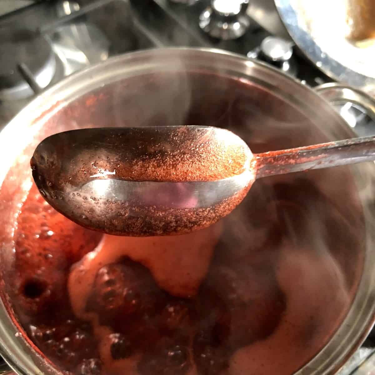 a spoon with homemade fruit sauce and a finger has swiped horizontally across the back of the spoon leaving a clean spot that the sauce is not dripping into