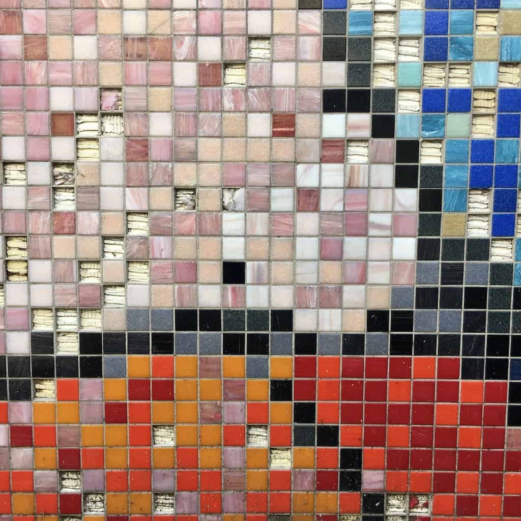closeup of a portion of a city wall with small mosaic tiles fanning out in a triangular pattern with blue, yellow, mauve, red, and grey tiles each section outlined in black (made to look like vintage computer graphics) -showing only the pink, red and blue sections