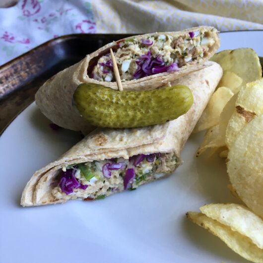 halved tuna fish salad wrap on a plate with plain potato chips, a pickle and pickled okra