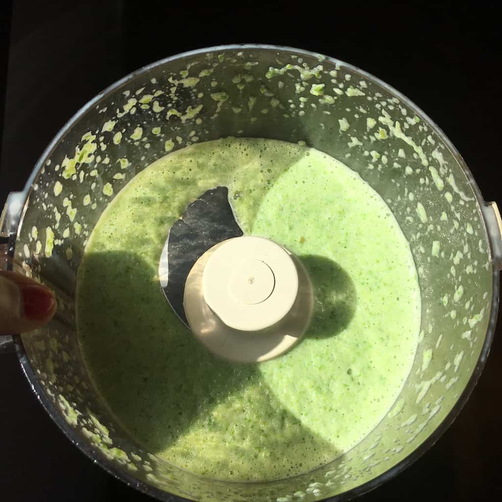 milk and blanched asparagus mixture in the bowl of a food processor in the sunlight looking beautifully spring green