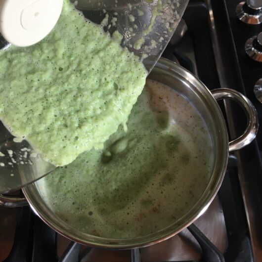 pouring spring green milk and blanched asparagus mixture into the remaining milk being heated on the stove