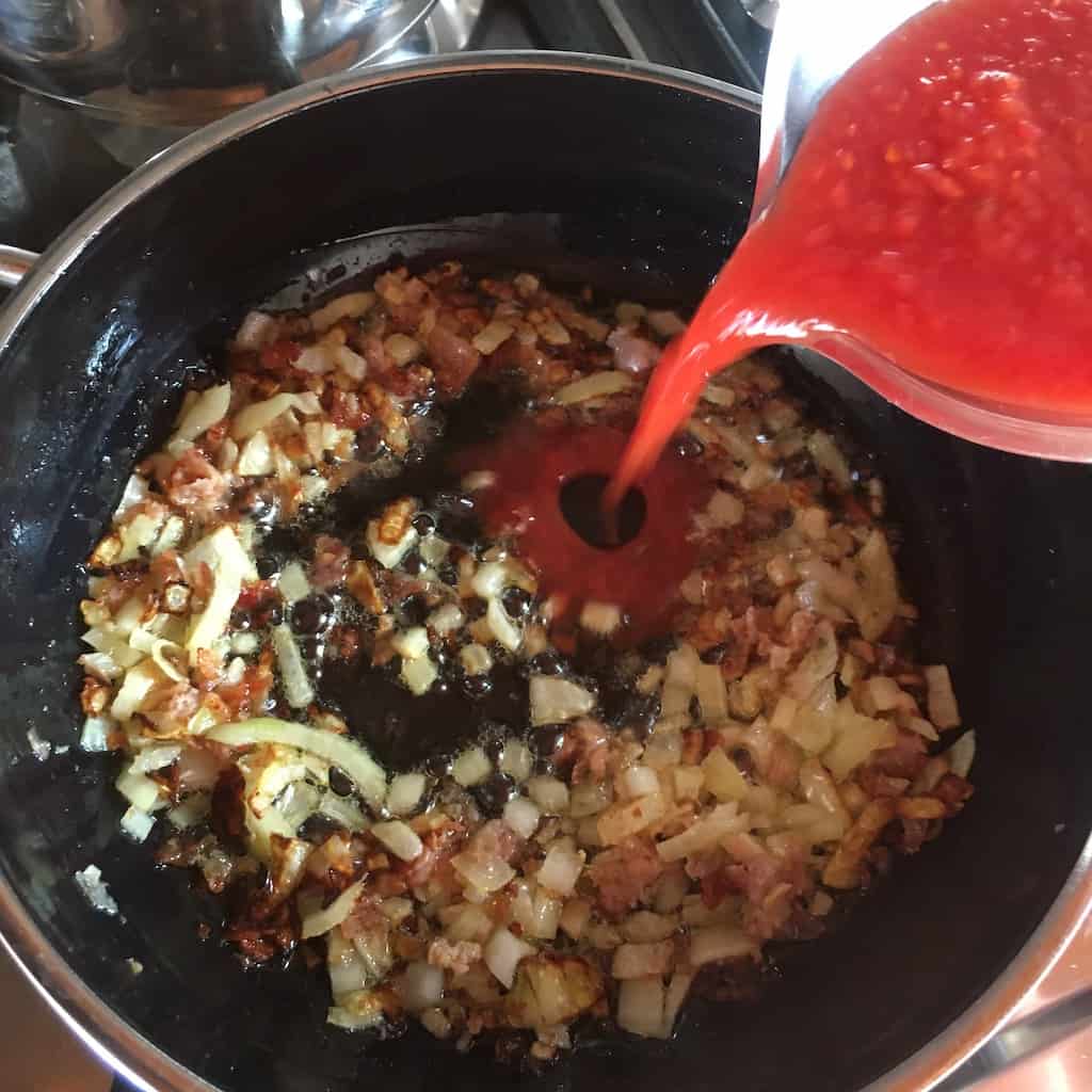 pouring tomato sauce int the pan with prosciutto and onions