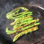 asparagus spears cooking in a cast iron skillet with smoke rising