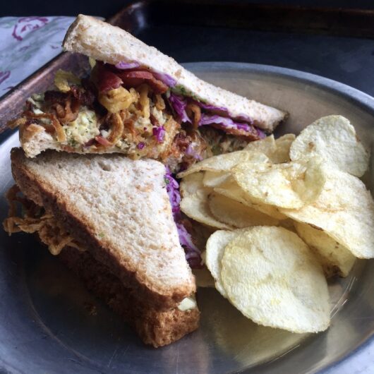 yellowfin tuna sesame scallion salad with crispy bacon, french fried Vidalia onions and purple cabbage strips on wheat bread with a side of plain potato chips in a vintage 9" pie tin with a tea towel with flowers in the background