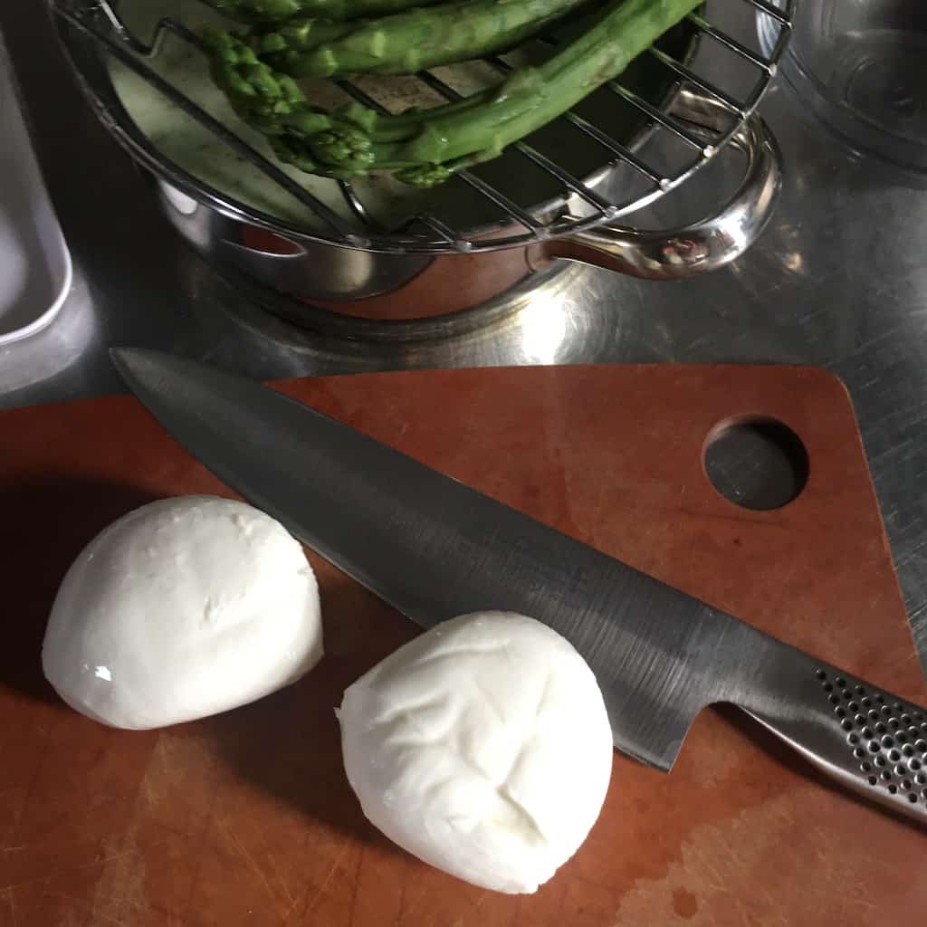 2 whole mozzarella balls on a cutting board next to my Global Brand chef's knife all lying on a cutting board