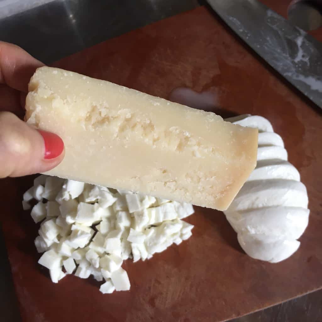 my hand holding a large chunk of hard cheese with mozzarella in the background