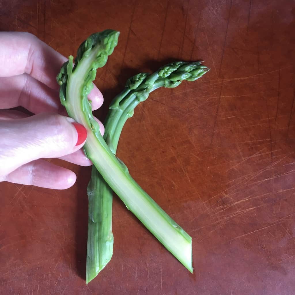 my hand holding a vertically sliced blanched asparagus spear