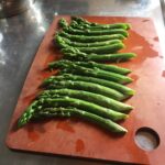 assembled asparagus spears lying on a cutting board with the spears curves opposing each other leading out to the left and right sides from the middle.