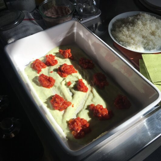 dots of bright dark red tomato sauce on top of the pale green bechamel sauce in a white ceramic lasagna dish