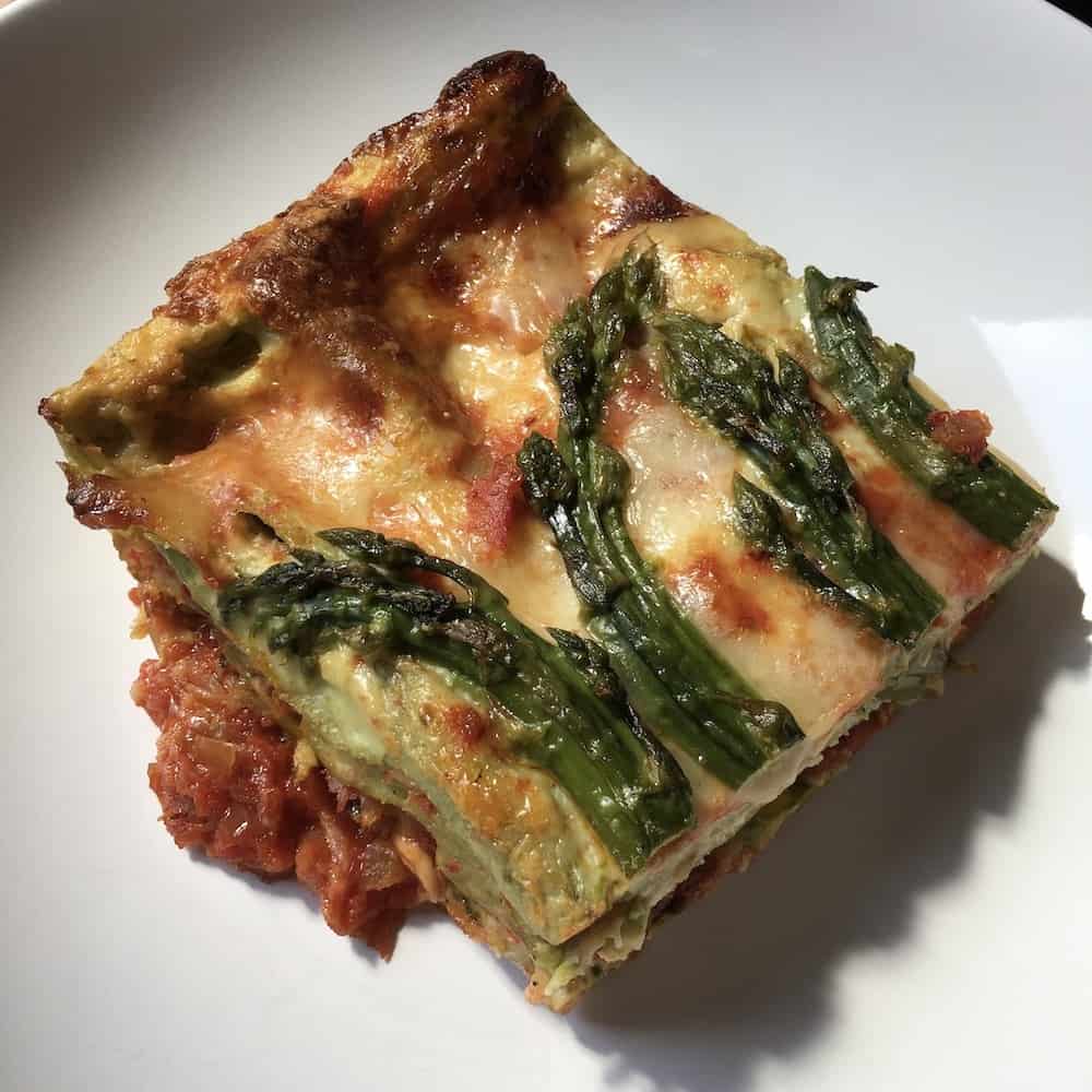 a large piece of cut asparagus Lasagna with prosciutto sauce underneath in a pasta bowl