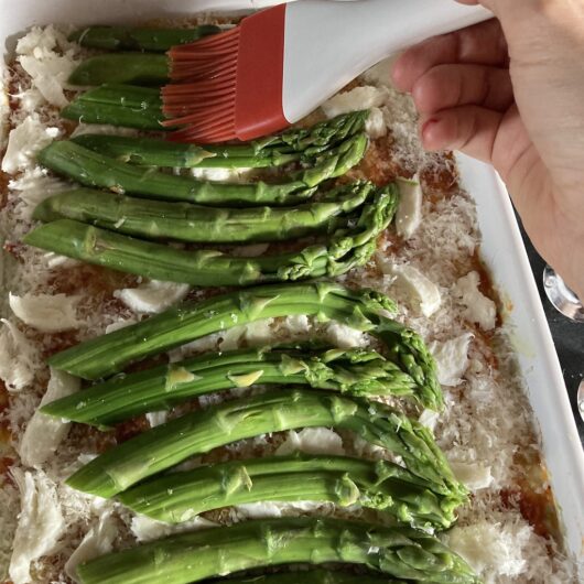 my hand brushing the asparagus lightly with olive oil using a silicone pastry brush