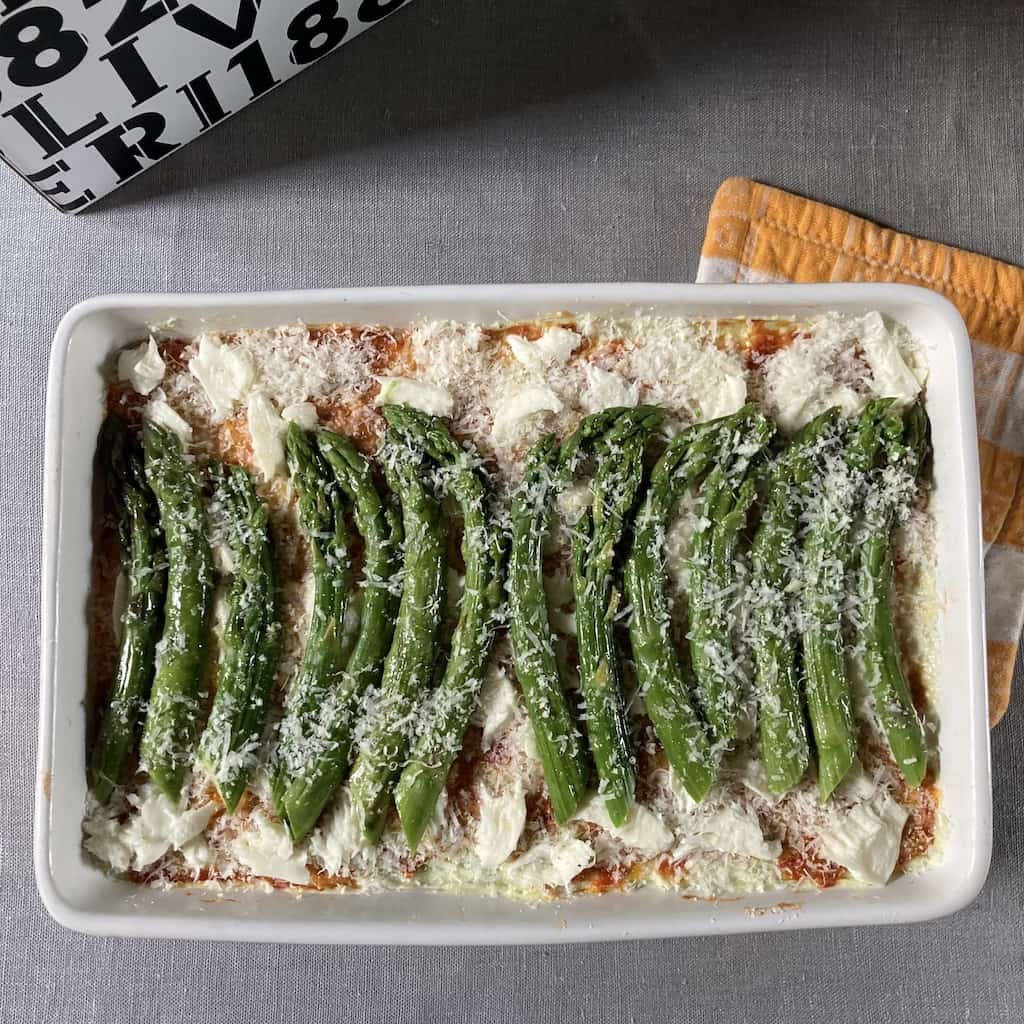 small amount of grated cheese on top of the asparagus ready to be covered and baked