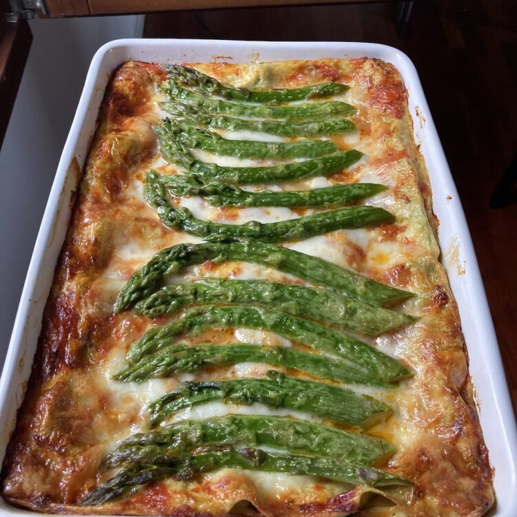 lasagna with asparagus on top in a white ceramic lasagna pan