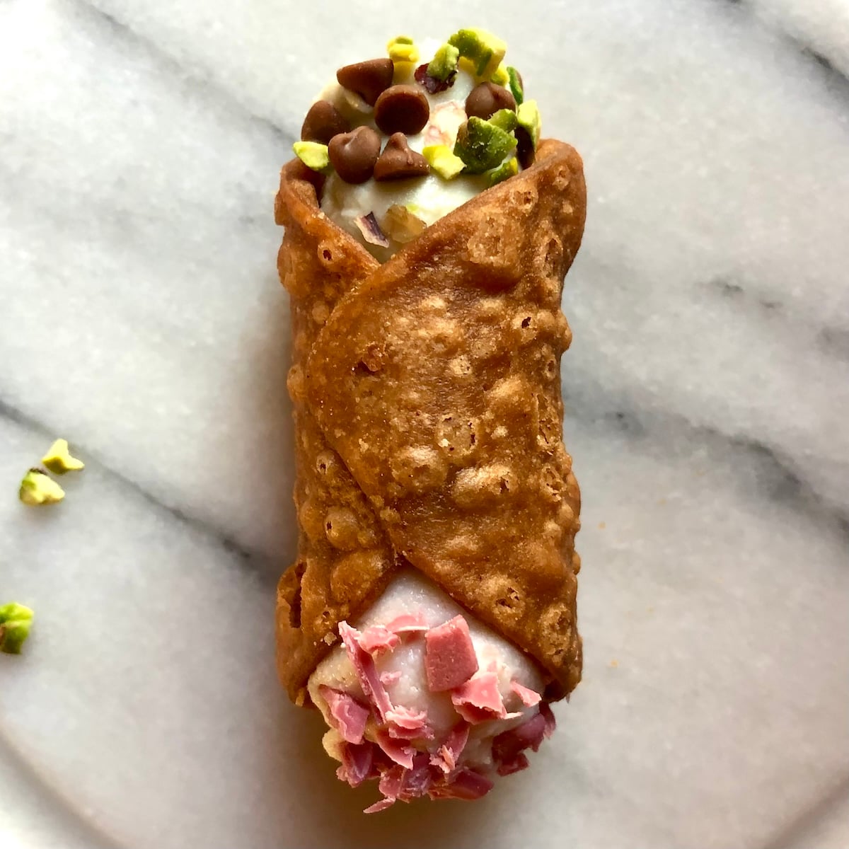Authentic, homemade Italian crispy cannoli filled with ricotta cream and dipped in toasted pistachios and strawberry white chocolate chips on the other end.