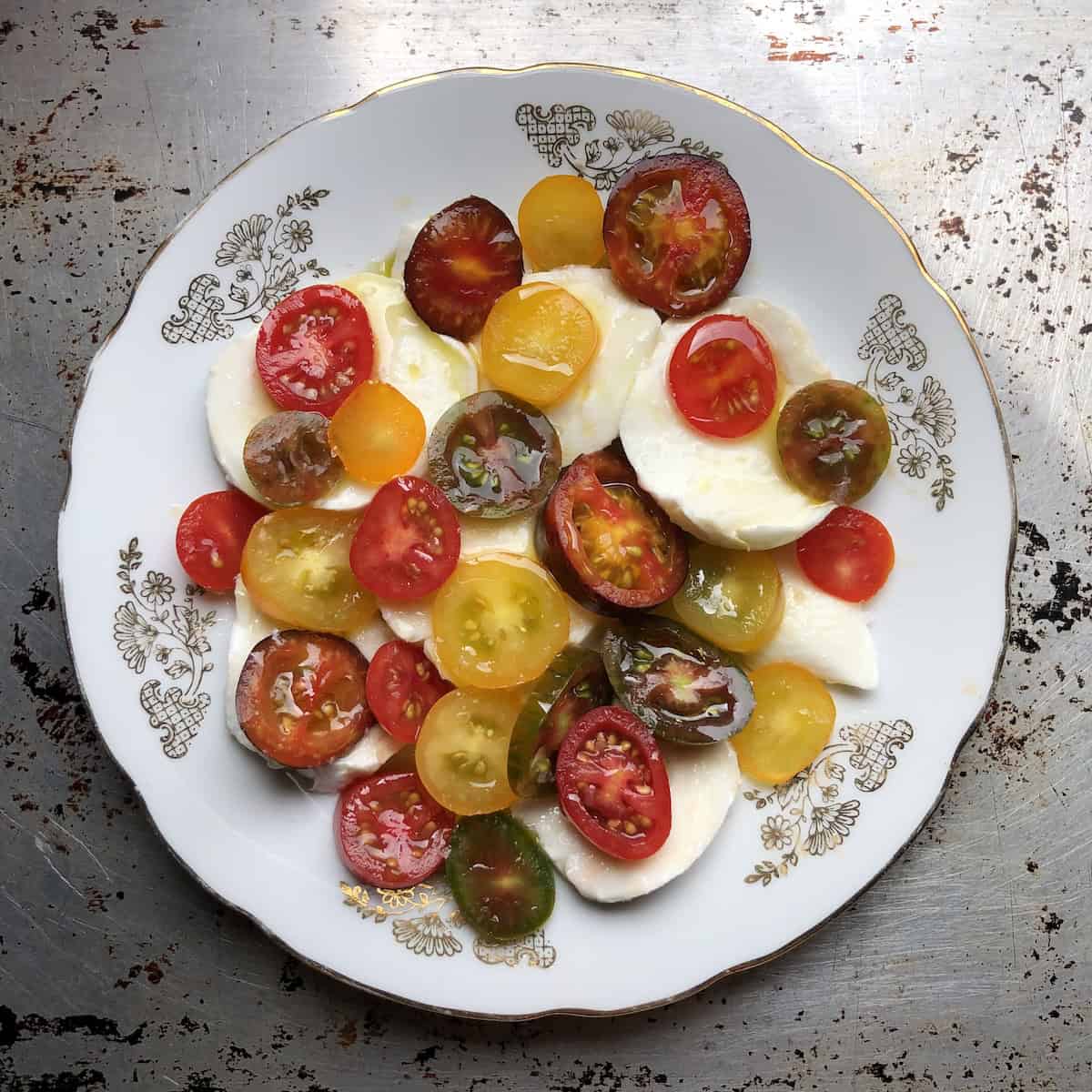 Grape tomato Caprese Salad (insalata Caprese) on a ceramic plate with green, red, and yellow grape tomato varieties.