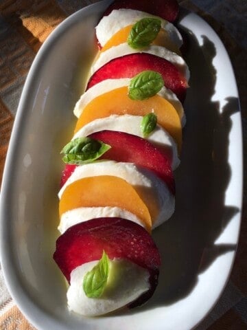 Homemade plum and mozzarella caprese salad with basil leaves, olive oil, and sea salt on a serving platter making one of the best unique caprese salad options ever!