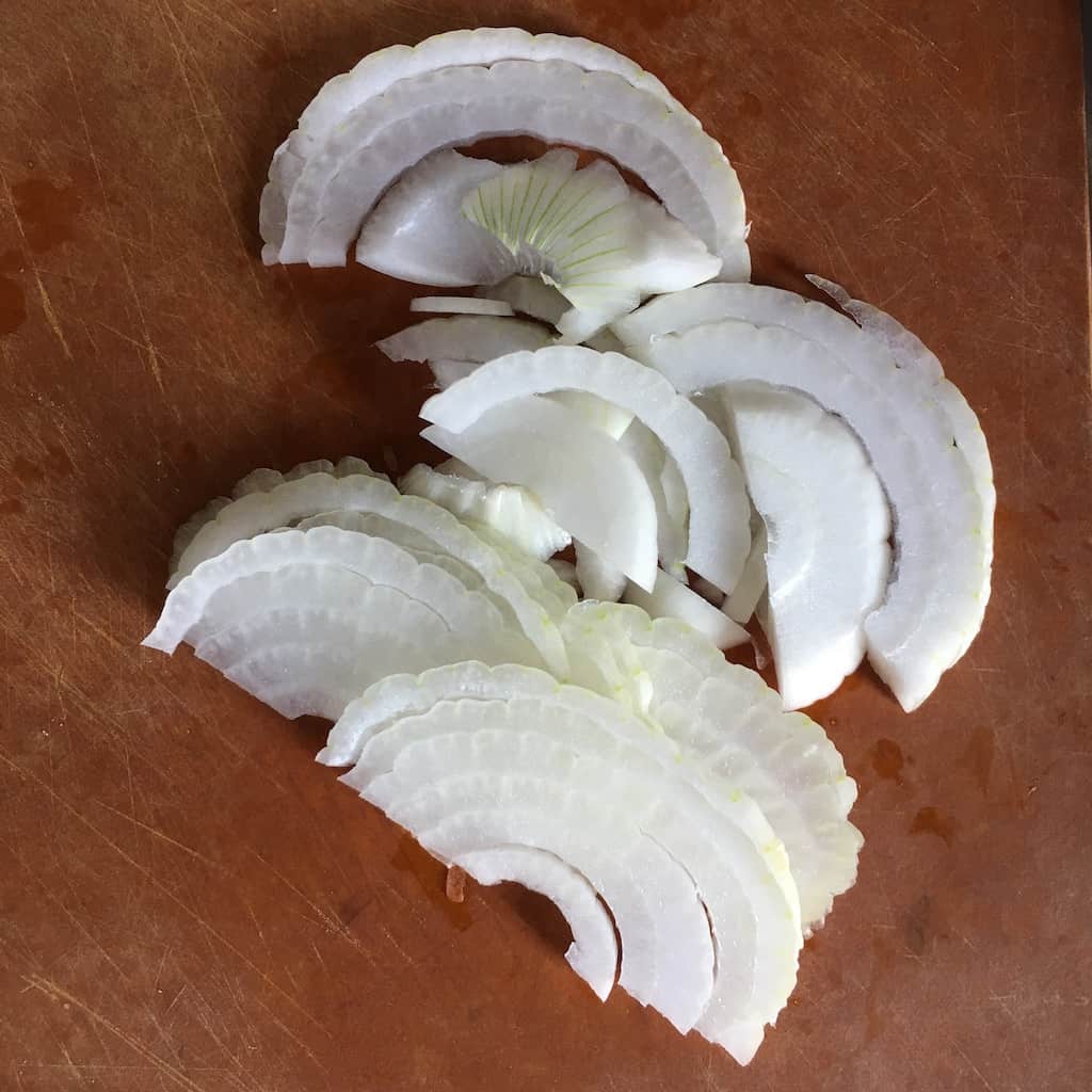 sliced onions on a cutting board that look like rainbow shapes because of how they've been sliced