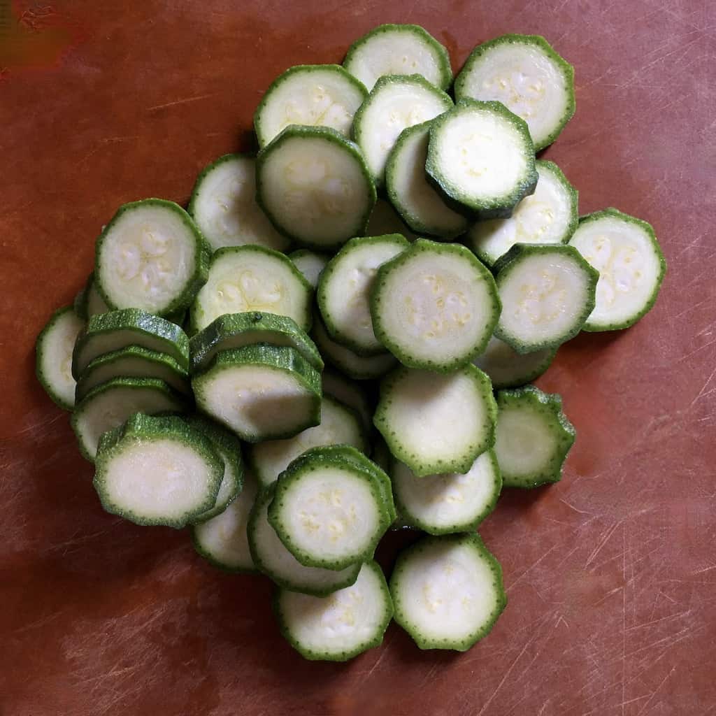 sliced baby zucchini rounds on a brown cuttaing board